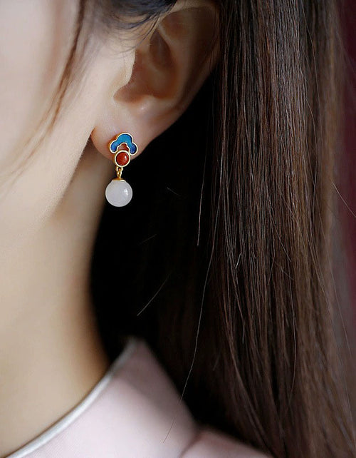 Woman wearing blue enamel red stone white pearl drop earrings as colorful dangle jewelry