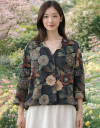Black long sleeve button down blouse with colorful vintage floral print laid flat over white skirt and woven bag