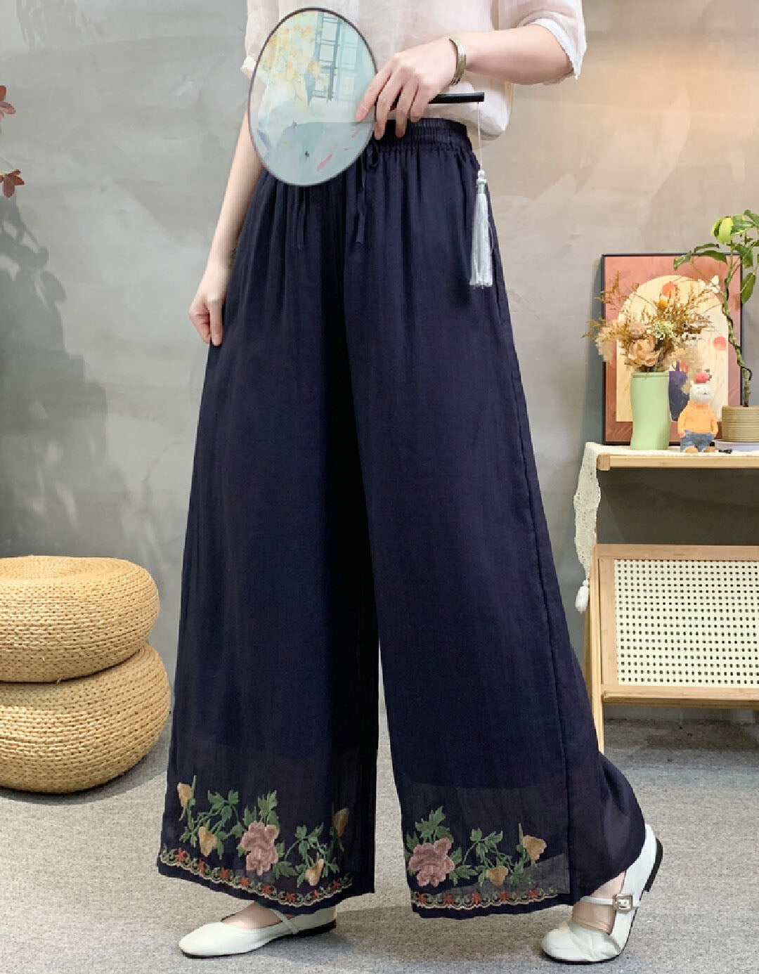 Person wearing dark blue wide-leg pants with floral embroidery in a room setting.