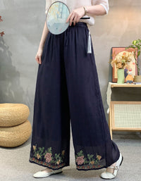 Person wearing dark blue wide-leg pants with floral embroidery in a room setting.