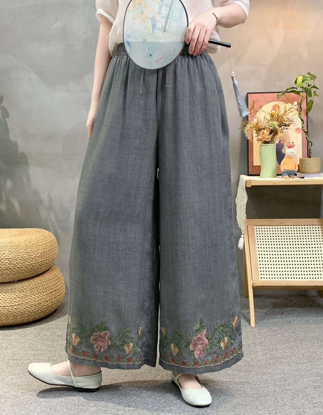 Loose linen palazzo pants in grey with colorful flower embroidery at cuffs, worn with flats front view