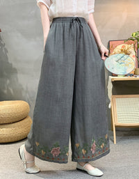Person wearing gray wide-leg pants with floral embroidery in a room setting.