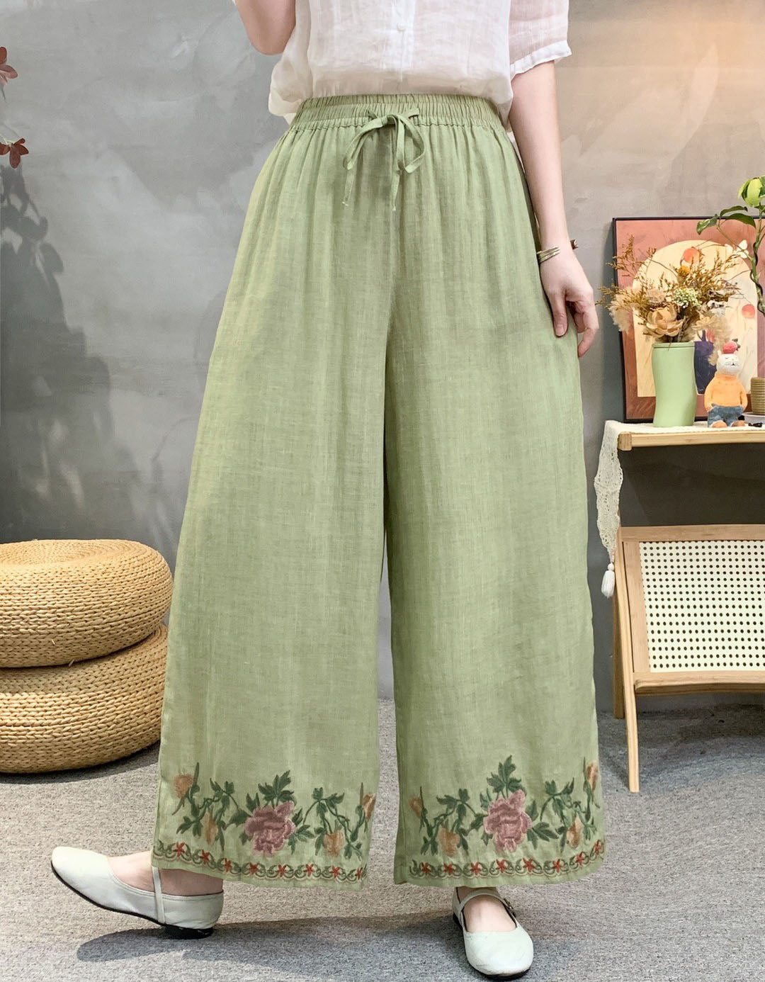 Loose linen palazzo pants in grey with colorful flower embroidery at cuffs, worn with flats.