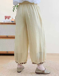 Person wearing light-colored pants with a subtle pattern, standing in a room with a wooden cabinet and plant.