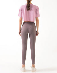 Person wearing a pink crop top and gray leggings on a white background full view