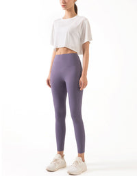 Person wearing a white crop top and purple leggings on a white background full view