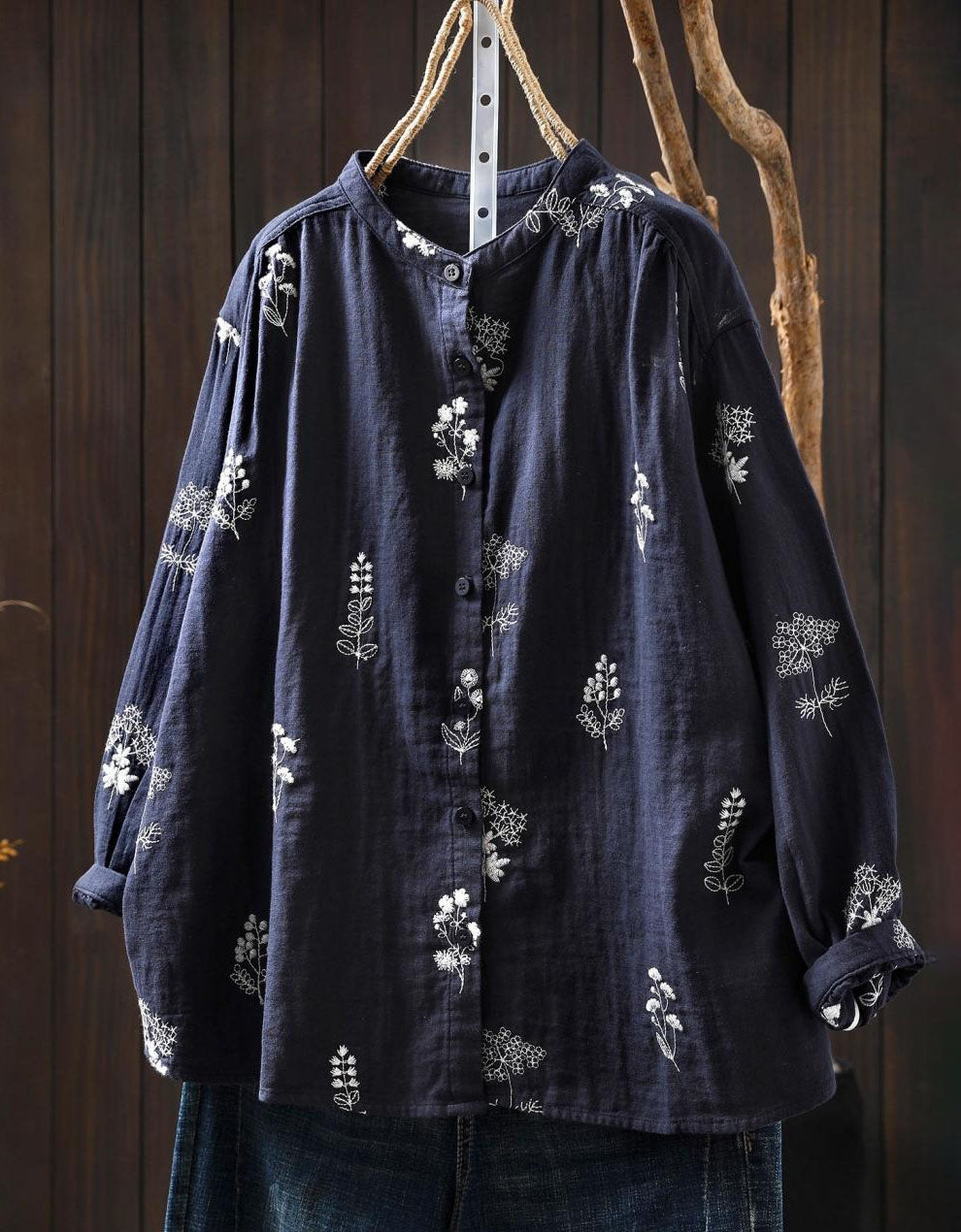 Navy blue shirt with white floral embroidery on a wooden hanger against a wooden background
