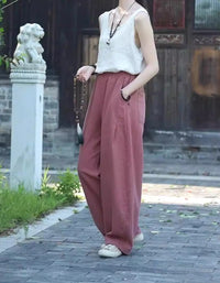 Person wearing a white sleeveless top and maroon wide-leg pants standing on a paved path.