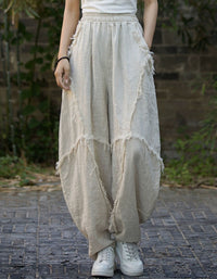 Person wearing beige distressed wide-leg pants and white sneakers on a brick path.