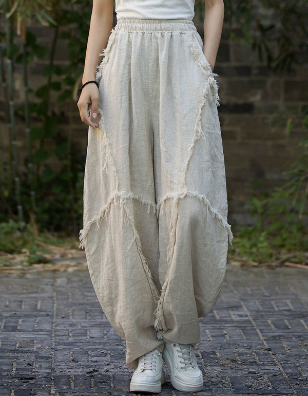 Person wearing beige distressed wide-leg pants and white sneakers on a brick path.