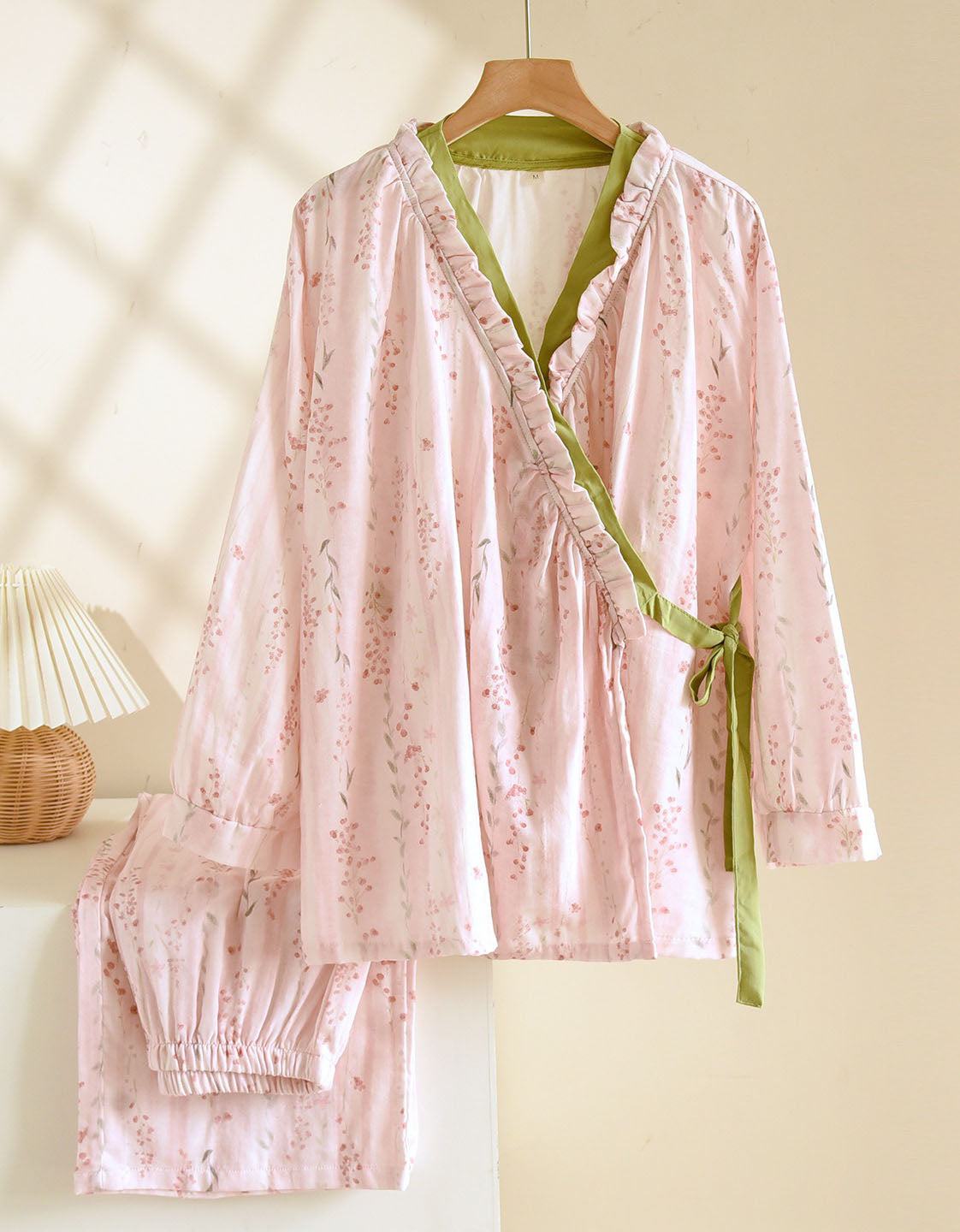 Pink floral pajama set with green trim on a hanger against a neutral background