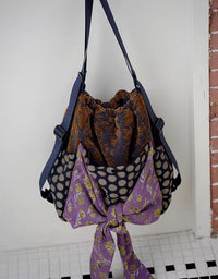 Multicolored fabric bag with a purple section featuring floral patterns on a white wall.