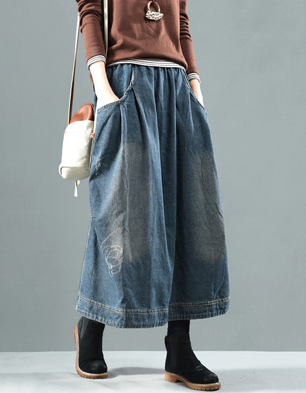 Person wearing a long denim skirt with a plain background