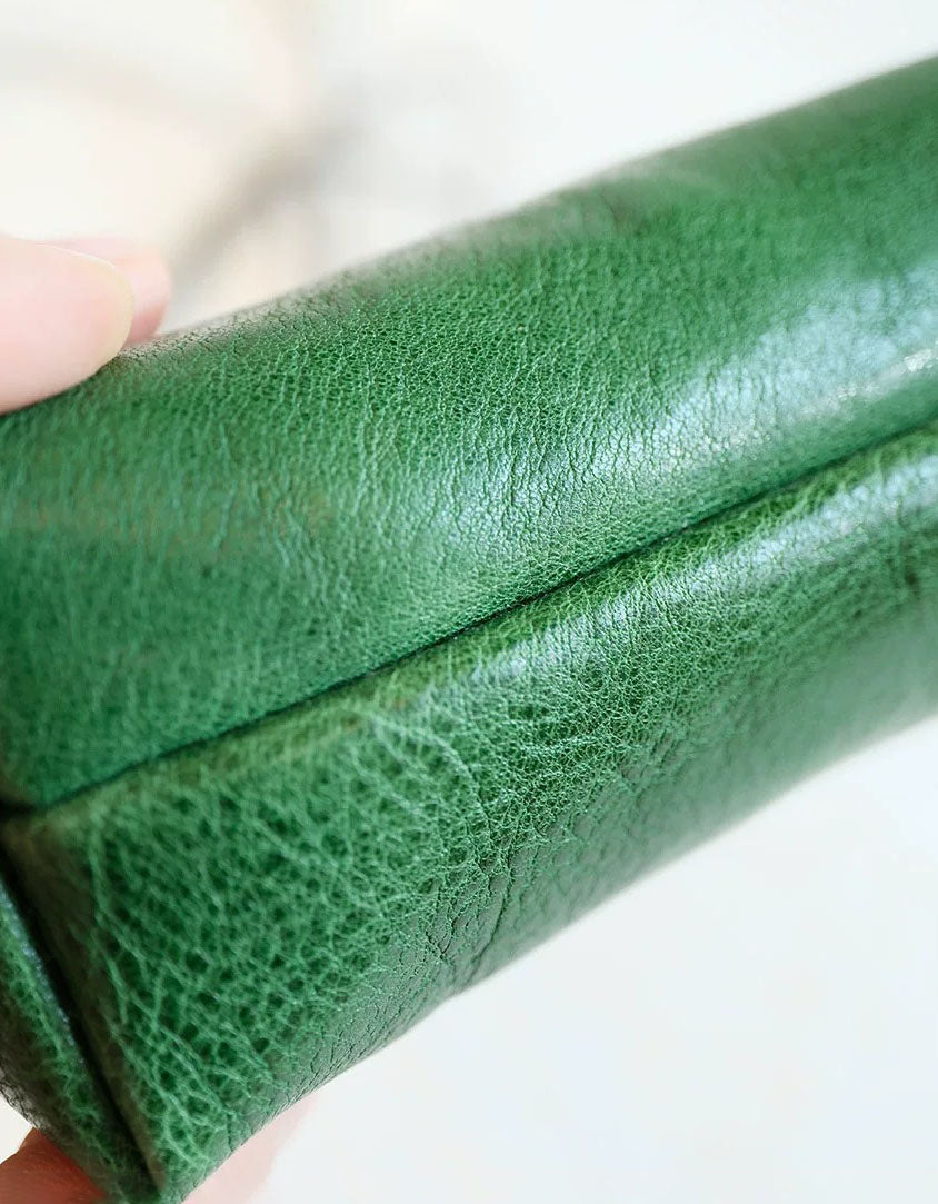 Close-up of a green leather-bound book held by a hand on a white background