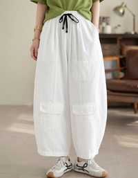 Model wearing white balloon pants with white sneakers in a minimalist room.