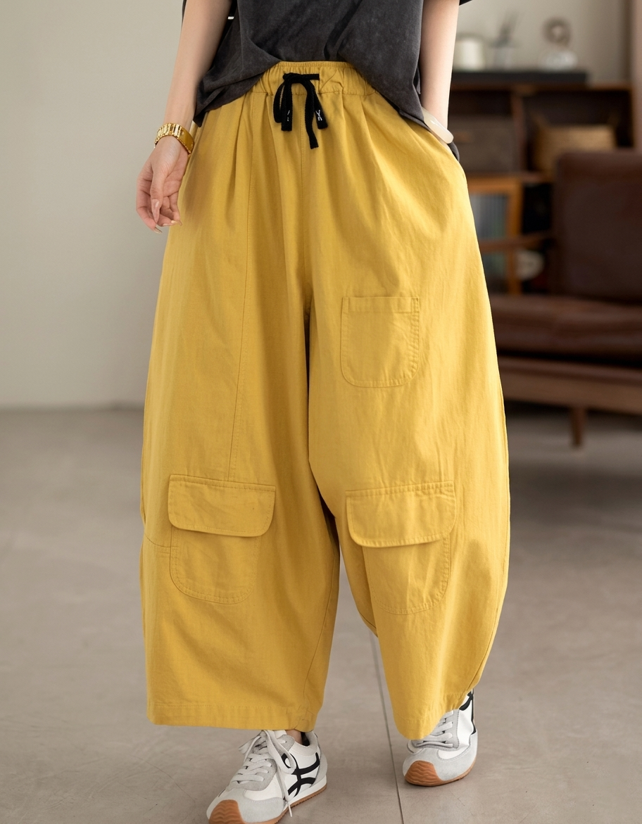 Model wearing ochre balloon pants with white sneakers in a minimalist room.