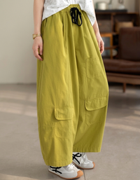 Model wearing green balloon pants with white sneakers in a minimalist room.