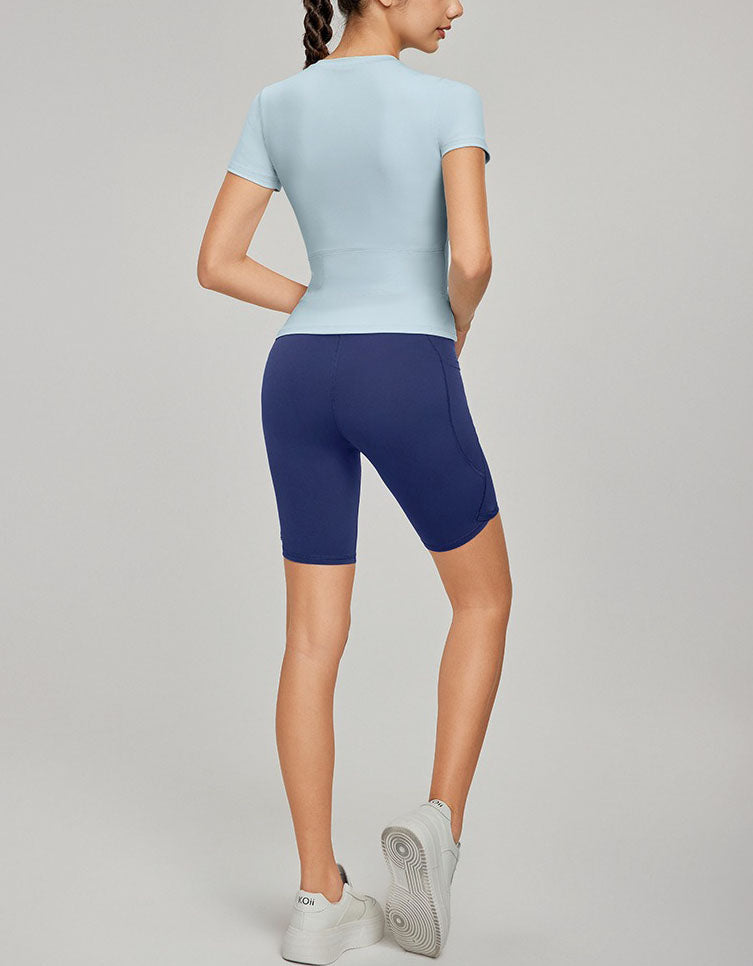 Person wearing a light blue athletic top and navy shorts on a gray background back view