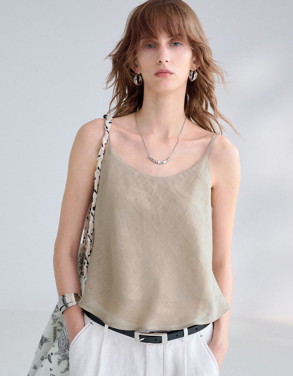Woman wearing a beige sleeveless top and white pants against a plain background
