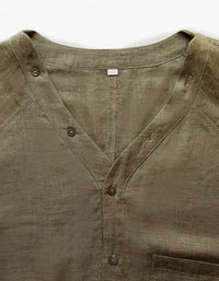 Close-up of relaxed olive linen V‑neck shirt with long sleeves and slightly cropped elastic hem.