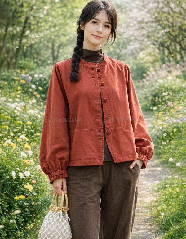 Woman in a rust-colored jacket standing in a garden with flowers and trees.