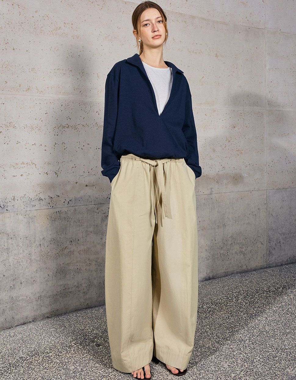 Person wearing a navy blue top and beige pants against a gray concrete wall.
