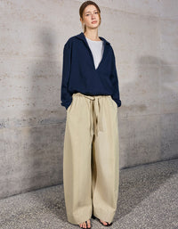 Person wearing a navy blue top and beige pants against a gray concrete wall.