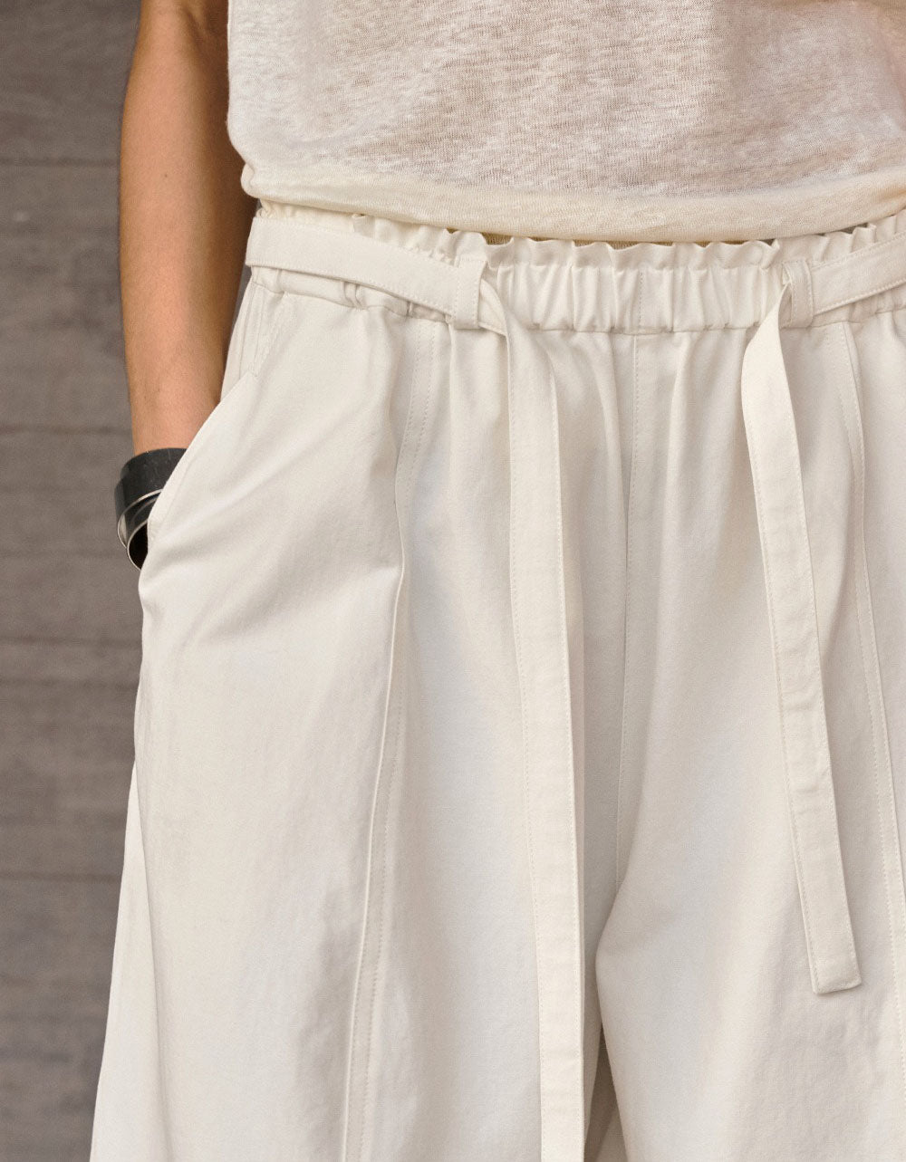 Close‑up of drawstring high waist and pleated front on beige wide leg trousers.