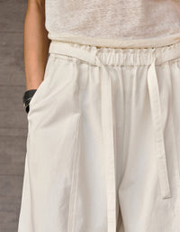 Close‑up of drawstring high waist and pleated front on beige wide leg trousers.