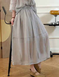 Person wearing a long light gray dress standing indoors with wooden flooring.