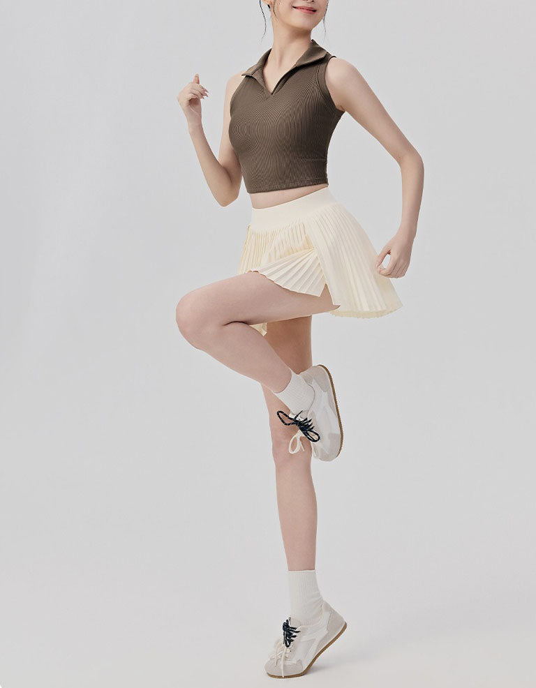 Person wearing a brown sleeveless top and beige pleated skirt on a plain background full view