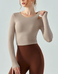 Woman wearing a beige long-sleeve top and brown leggings against a light gray background