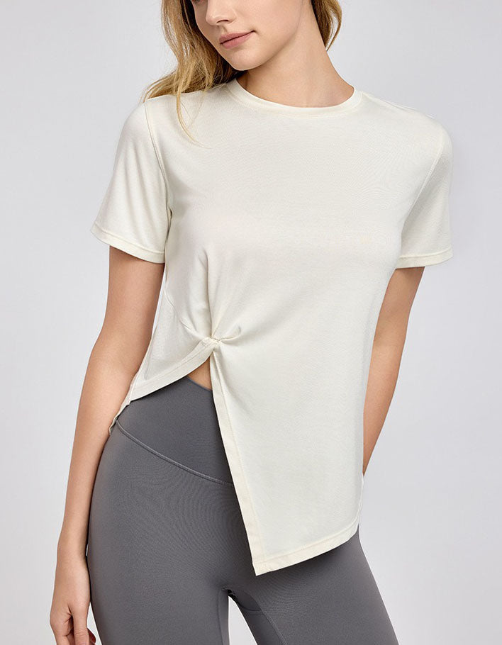 Woman wearing a white short-sleeve top with a knot detail and gray leggings on a light gray background