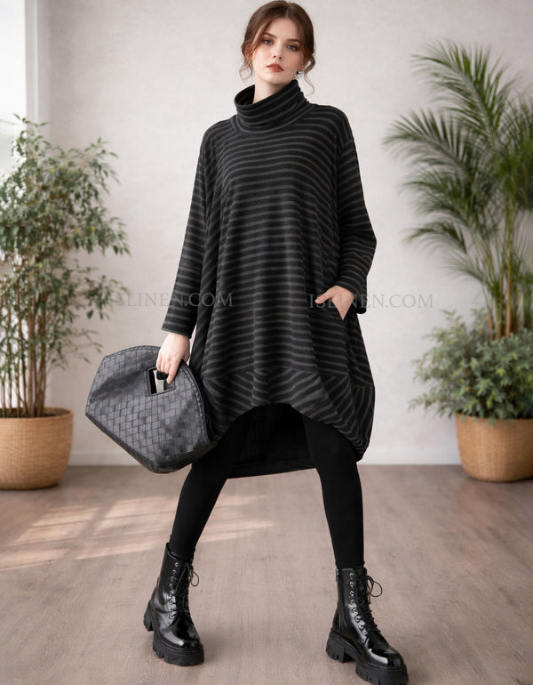 Woman wearing a black striped dress with black tights and boots, holding a gray bag indoors.