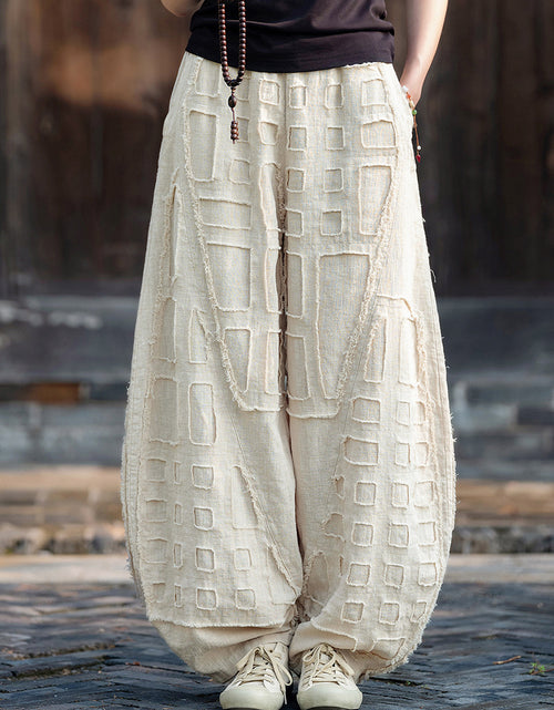 A pair of beige ramie linen harem pants featuring a geometric patchwork design, displayed on a model.