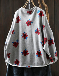 Gray sweater with red and blue floral patterns hanging against a wooden background