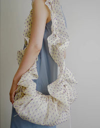 Woman carrying cream ruched ruffle scrunchie shoulder bag with tiny purple print over blue dress