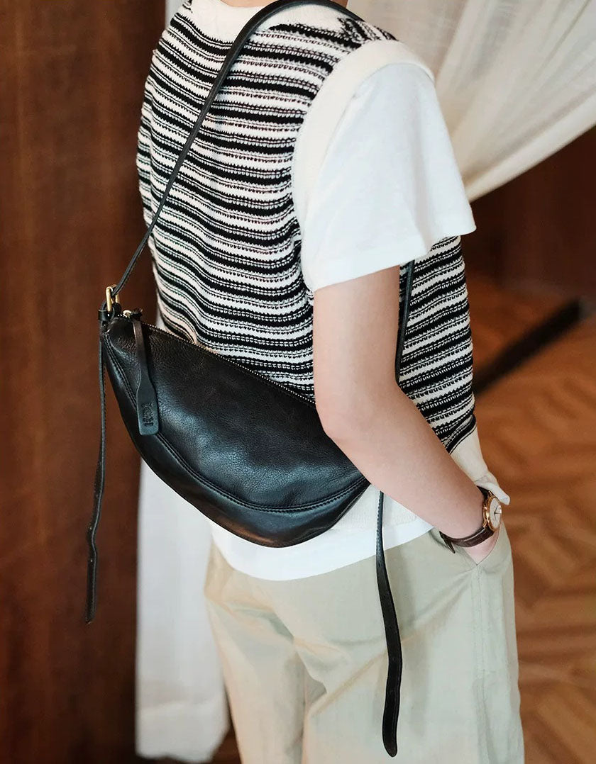 Woman wearing black half moon shoulder bag with casual striped knit top and beige shorts