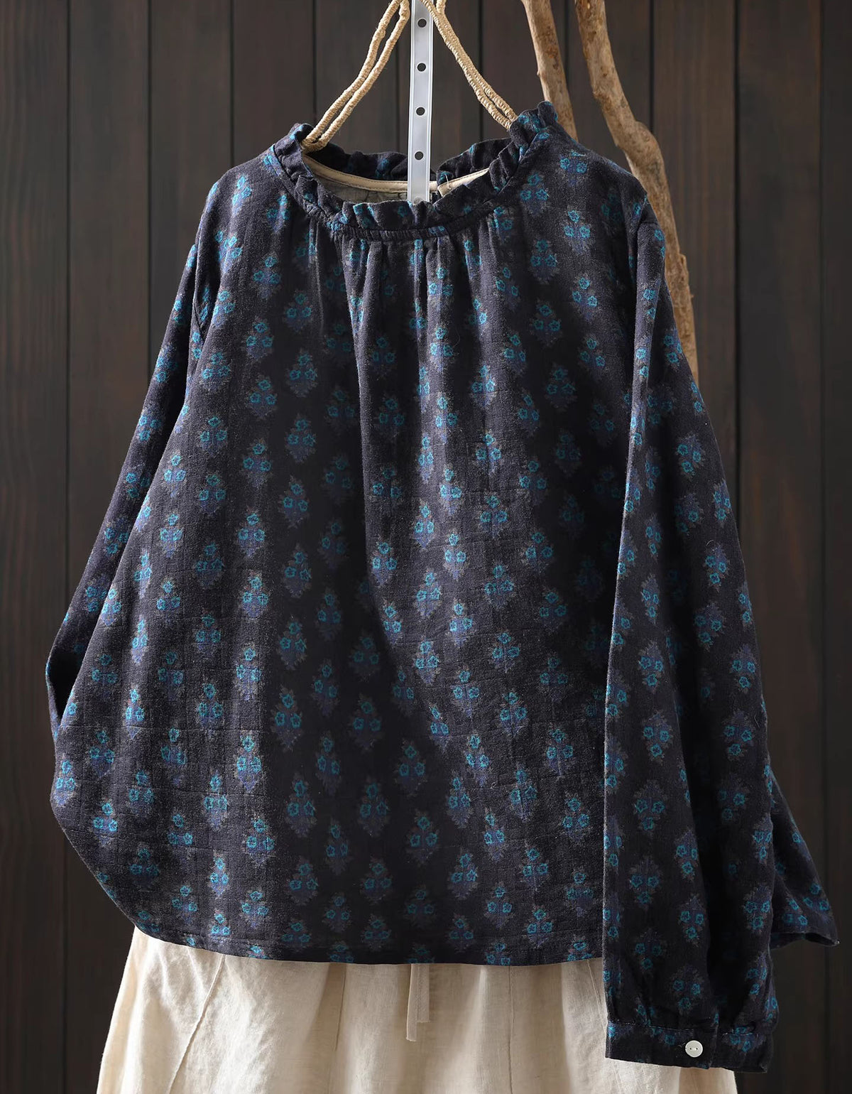 Dark patterned blouse with long sleeves on a wooden hanger against a dark wooden background