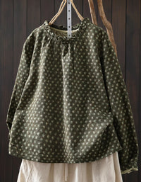 Green patterned blouse with long sleeves hanging on a wooden hook against a dark wooden background.