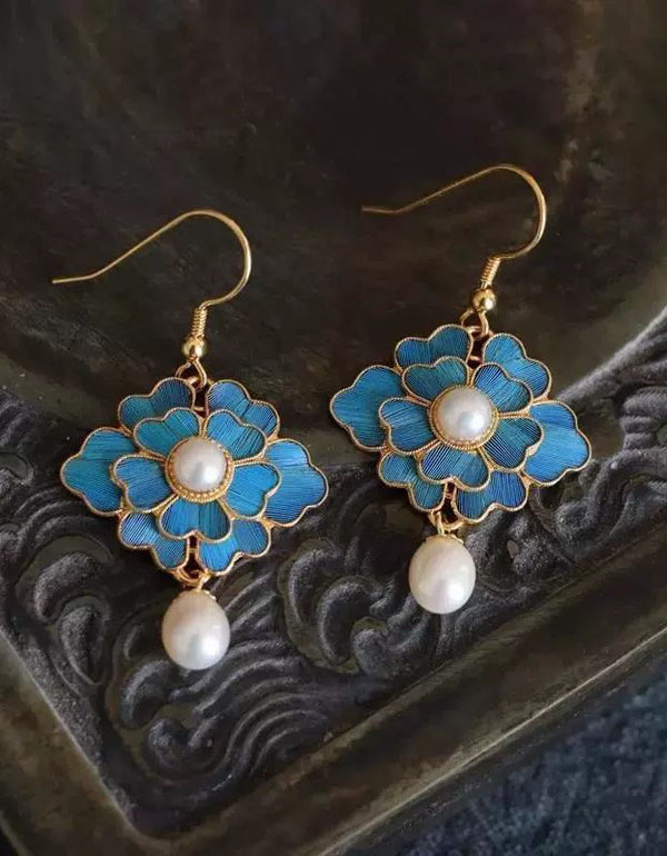 Pair of blue floral earrings with pearl centers on a textured dark background