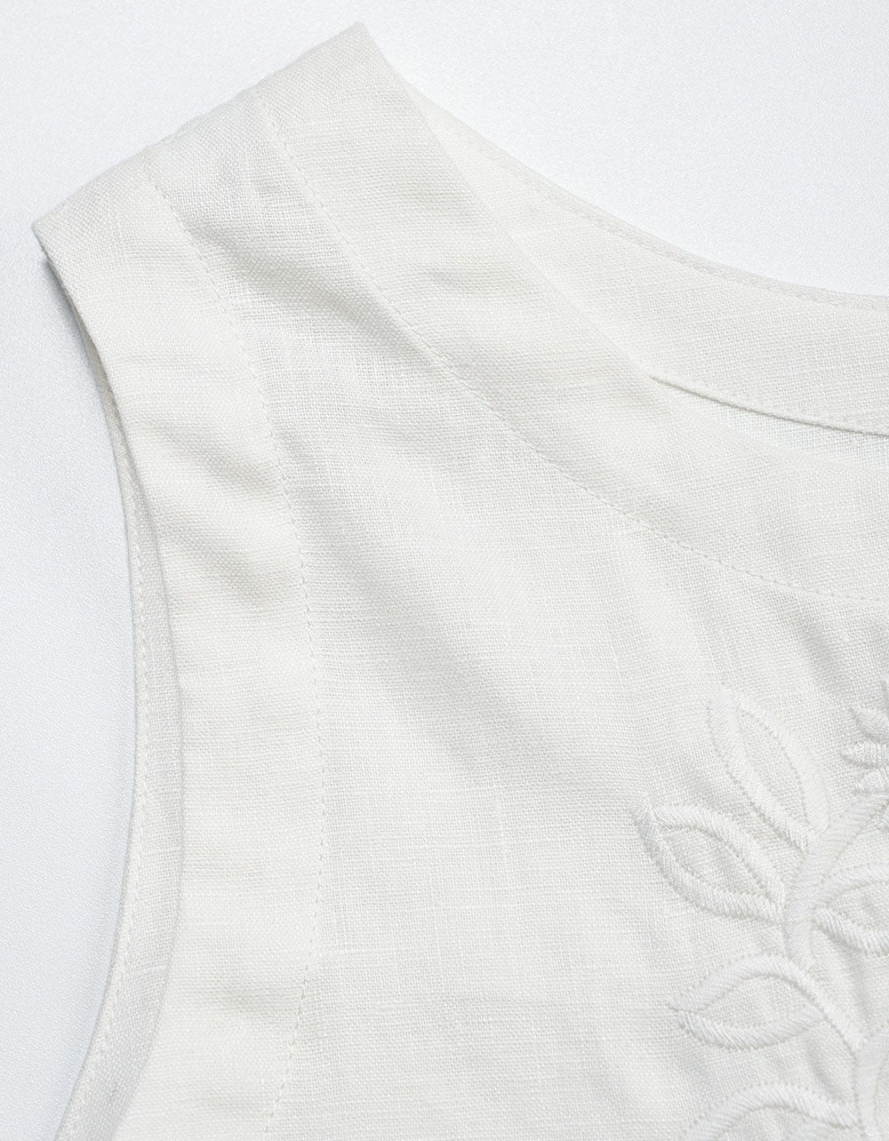 Close-up of a white sleeveless top with textured pattern on a light gray background