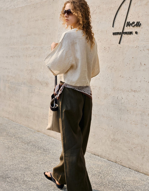 Woman wearing boxy beige linen top with wide sleeves styled with olive pants and patterned scarf for a relaxed summer look.