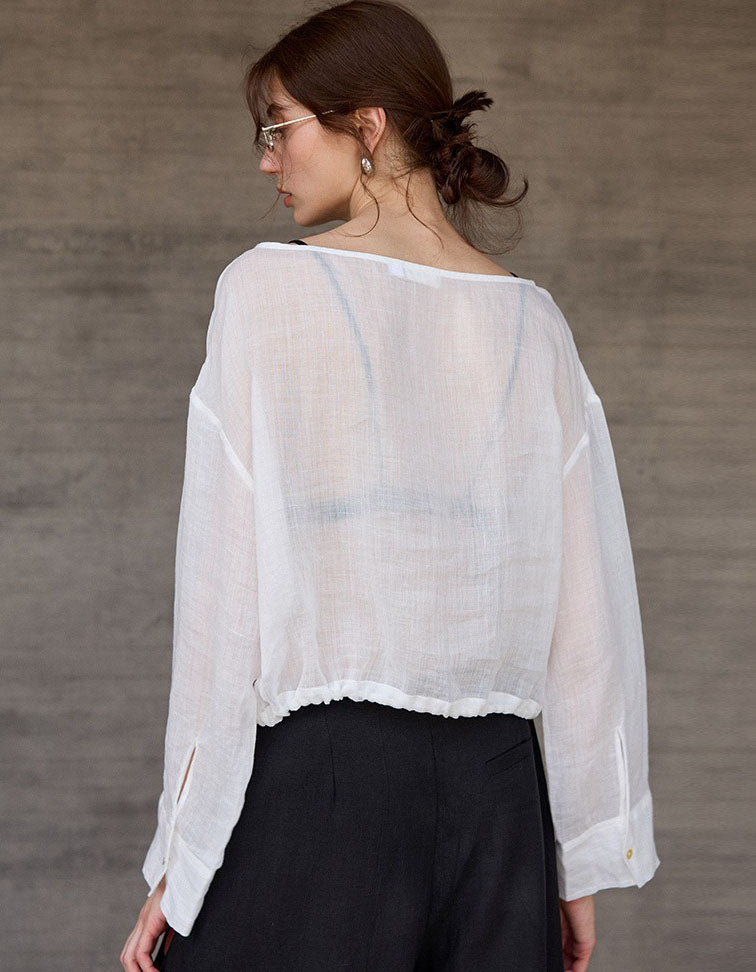 Woman wearing a sheer white blouse over black pants against a gray background