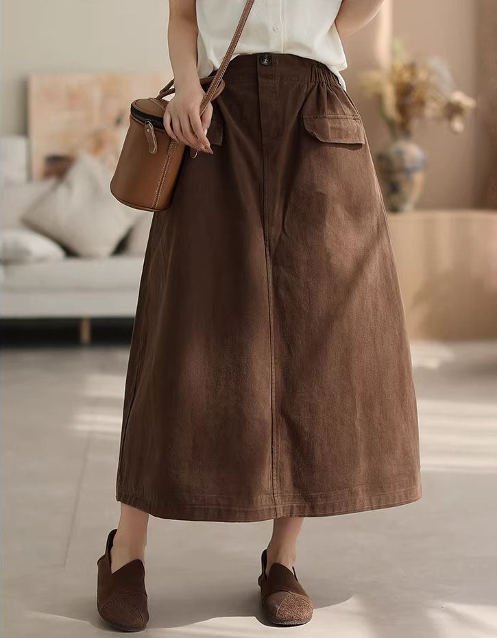 Person wearing a brown skirt and holding a brown bag in a neutral setting