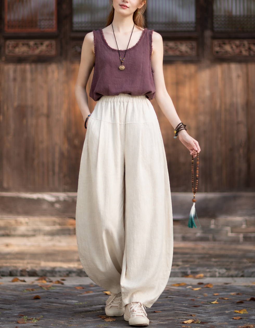 Beige linen harem pants with high elastic waist and lantern legs, worn with brown top and sneakers outdoors.