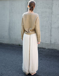 Person wearing a beige blouse and white pants standing against a concrete wall.