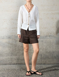 Person wearing a white blouse and brown shorts against a concrete wall.