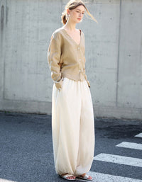 Woman wearing a beige cardigan and white pants standing on a street.