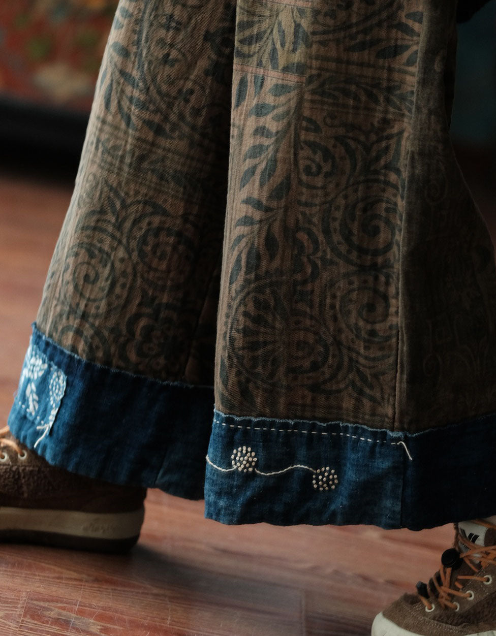 Close‑up of dark blue contrast hem with stitched floral detail on brown ethnic print wide leg pants